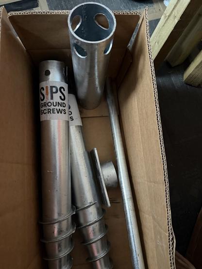 Two galvanised metal ground screws with the installation tool sitting in the box they just arrived in. New DIY inbound!