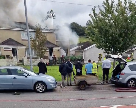 Thick smoke rises from the roof of an end‑terrace property in Neath as firefighters remain on scene at the major Furnace Terrace blaze.