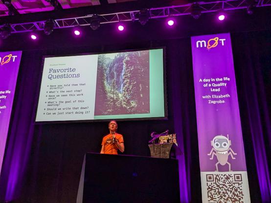 Elizabeth Zagroba on a stage in front of a slide with her favorite questions:
- Have you told them that directly?
- What's the next step?
- Have we seen this work once?
- What's the goal of this meeting?
- Should we write that down?
- Can we just start doing it?