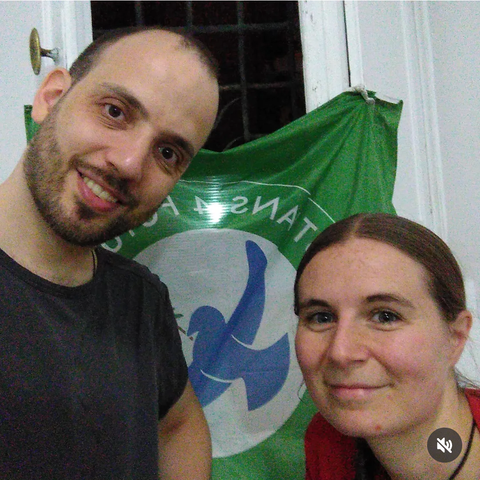 Ein Mann und eine Frau schauen lächelnd in die Kamera. Im Hintergrund ist die Flagge von Christians for Future.