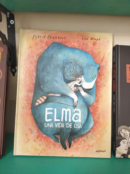 Imagen de la portada: con fondo naranja, ha dibujado un suelo otoñal, con un gran oso azul que está tumbado hecho un ovillo y que abraza a una niña pequeña, que a su vez abraza al oso. 
El título "Elma una vida de osa" está puesto en la parte de las patas traseras del oso en letras blancas.