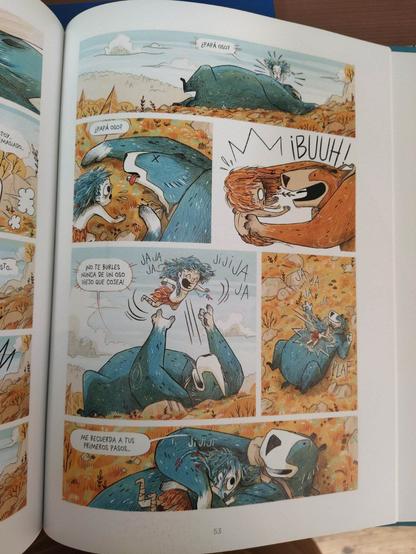 Fotografía de una de las páginas del libro. Hay viñetas con fondos naranjas, y el oso azul. La niña llama a papá oso creyendo que está muerto, hasta que él reacciona para asustarla. Después el oso se tumba boca arriba y juega felizmente con Elma,