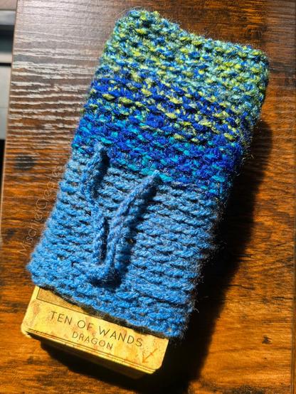 A crochet tarot card pouch that is blue and green. It has cards sticking out, with the Ten of Wands on top.