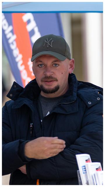 Christoph Biermann
1. Beisitzer / Wahlkampfkoordinator des AfD Kreisverband Göttingen. 

Ein Mann mit Kinn und Schnurrbart und 'NY' Baseball Kappe. 

Vorne im Bild unschwarf Infoständer der Partei. 

Um das Bild ist ein kleiner weißer Rahmen.