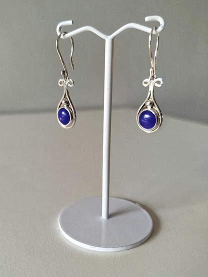 a pair of dangle drop silver earrings with a round blue stone. they are hanged from in white wire