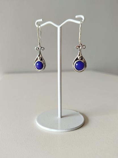 a pair of dangle drop silver earrings with a round blue stone. they are hanged from in white wire