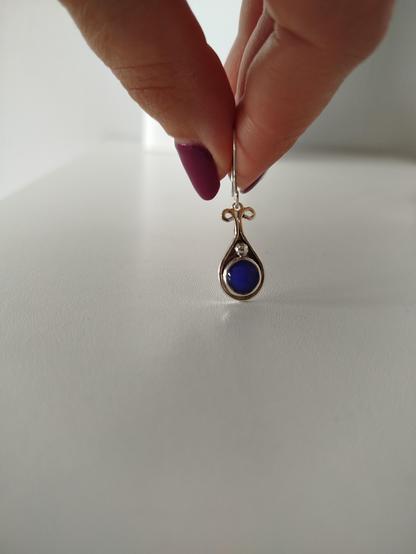 a dangle drop silver earring with a round blue stone. it's holded in fingertips
