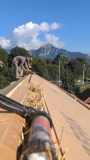 Deux charpentiers posant une plaque de bois sur faîtage de toiture
