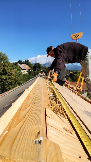 Un charpentier prend une mesure sur le faîtage d'un toit