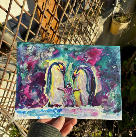 Illustration mit Buntstiften und Aquarellfarben von einer Kaiserpinguin-Familie. Die Eltern schauen auf das in der Mitte stehende Küken herunter.