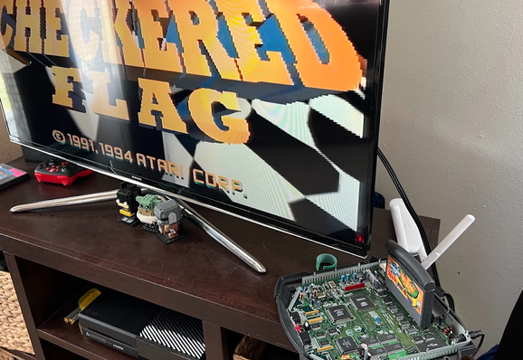 Atari Jaguar console with exposed inner motherboard playing a Checkered Flag cartridge with the game's logo showing on an adjacent TV.
