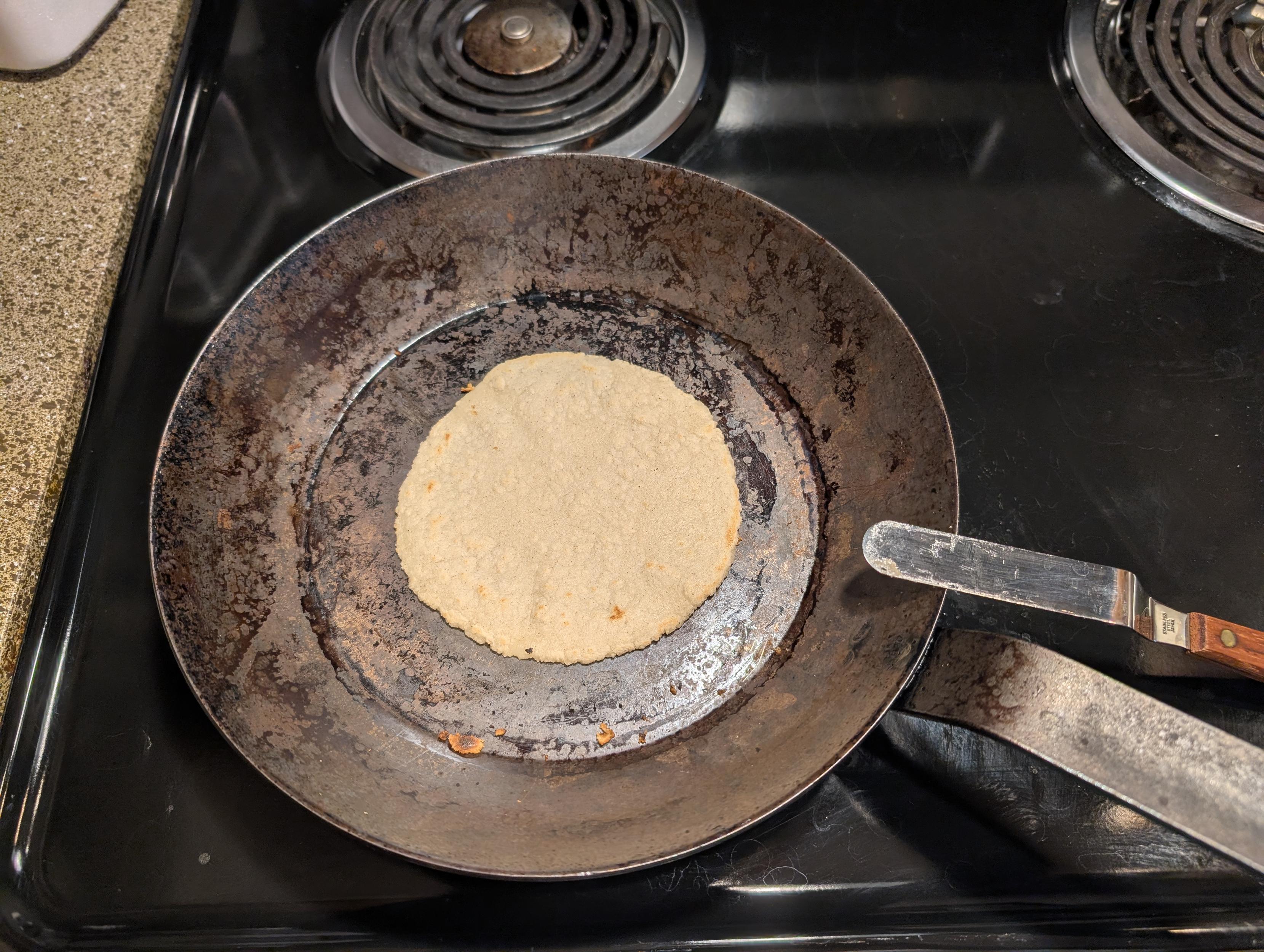 Corn tortilla being made on a grody carbon steel pan