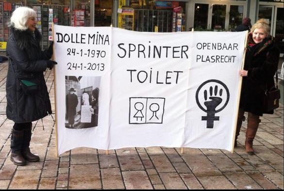 2 vrouwen met spandoek tussen hen in waarop Dolle Mina 1970-2013, sprinter toilet, openbaar plasrecht