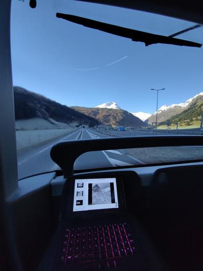 Front seat view from the top of a double decker post auto bus. On my lap a pocket reform computer. Outside the St. Bernardino pass mainbroad road with white mountains top.