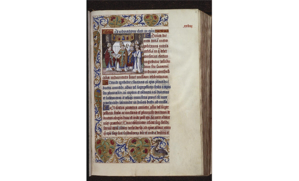 Page de manuscrit sur parchemin. Elle est organisée en plusieurs parties : à droite, une grande marge laissée vide (avec simplement une inscription en rouge en haut) ; un texte en rouge et bleu au centre ; une bordure ornée de motifs végétaux stylisés et de coeurs dorés avec des fraises. En haut à gauche du texte, une petite enluminure avec plusieurs personnages (des ecclésiastiques) réunis devant un autel