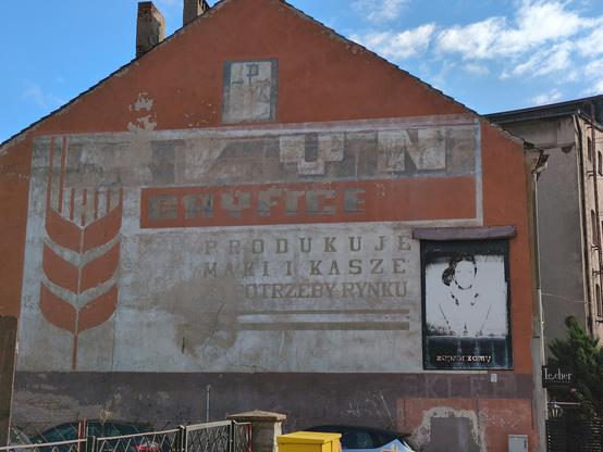 Wyblakły czerwono-szary mural na ścianie budynku pomalowanego na czerwono. Mural na planie prostokąta z jasnym (być może oryginalnie białym) tle. Po lewej stronie na czerwono symbolicznie przedstawiono zboże. U góry jasnymi literami na ciemniejszym tle szeroki napis "młyn". Poniżej szary na czerwonym pasie "Gryfice". Dalej ciemnymi literami na jasnym tle "produkuje mąki i kasze [na] potrzeby rynku". Po prawej wyblakła podobizna kobiety w czarnej ramce z brązowym "daszkiem" — widać zarys twarzy na tle ciemnych włosów spiętych z prawej strony i rzęs, oraz ślad ciemniejszych pasów sukienki. W dolnej części rzeczonej podobizny nieczytelne białe napisy i ledwie widoczne godziny otwarcia. Poniżej na czarnym tle napis "zapraszamy". Powyżej muralu ledwie widoczne "PZŻ".