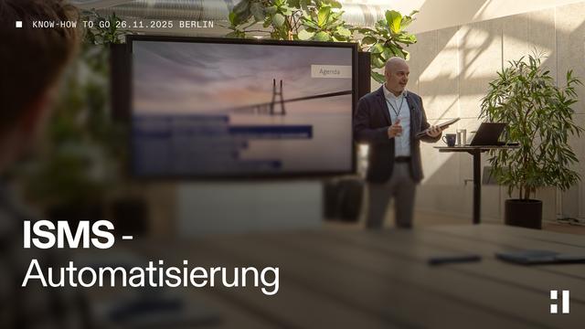 Ein Redner präsentiert im hellen, modern eingerichteten Konferenzraum in Berlin am 26. November 2025 zum Thema „ISMS-Automatisierung“. Auf einem großen Bildschirm ist die Agenda mit einem Brückenmotiv zu sehen. Der Raum ist mit Pflanzen dekoriert, auf dem Tisch liegen Stifte und Notizblöcke.