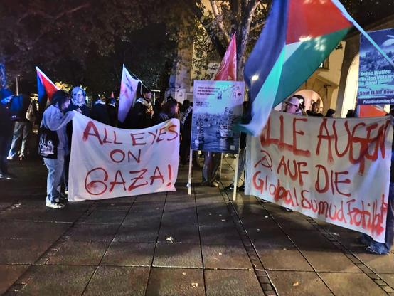 Eilkundgebung Abends in Stuttgart auf den Schlossplatz. Es sind große Palästina-Fahnen zu sehen und 2 weiße Banner mit der roten Schrift:
"ALL EYES ON GAZA!" und "ALLE AUGEN (Hammer und Sichel) AUF DIE Global Sumud Flotilla"