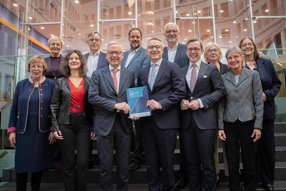 Gruppenfoto: Mitglieder des Nationalen Normenkontrollrats, Minister Wildberger und Staatssekretär Philipp Amthor stehen zusammen und präsentieren die Broschüre des Jahresberichts des NKR.