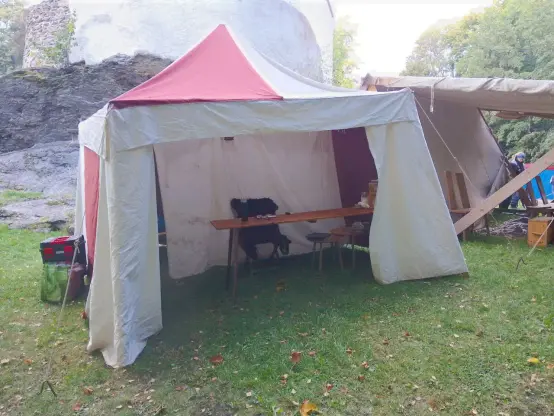 Ein offenes rotbraun-weißes Zelt steht vor der kleinsten Burg Sachsens, vor der Burg Rabenstein in Chemnitz. Der braune Tisch im Zelt ist noch nicht fertig dekoriert; hinter dem weißen Stoff in der Mitte des Zeltes ist der Schlafplatz versteckt.