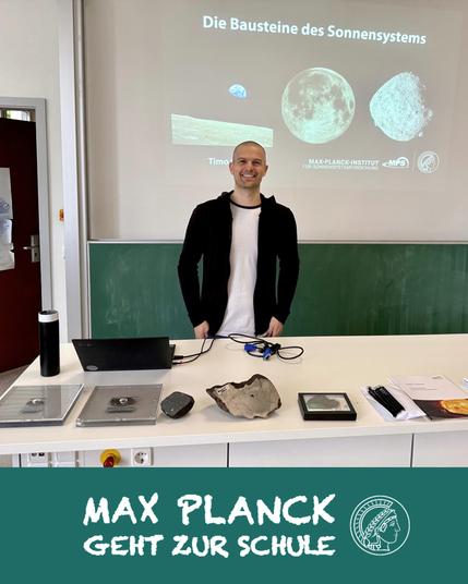 meteorites and other samples arranged on a table before a blackboard with a scientist