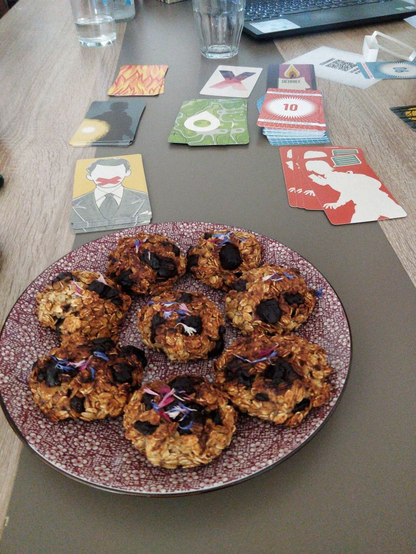 Une table, avec des cartes de jeu et une assiette de cookies recouvert de fleurs