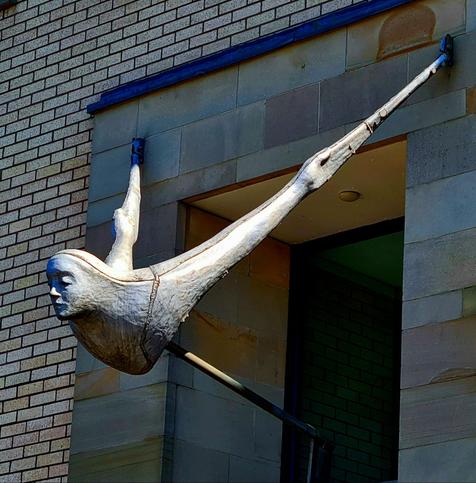 A sculpture consisting of a torso and arms leaning outwards above the entrance to a building.