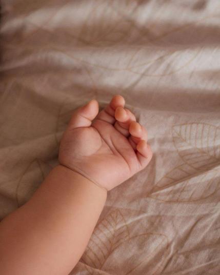 A baby’s hand, outstretched, resting on soft, natural sheets.