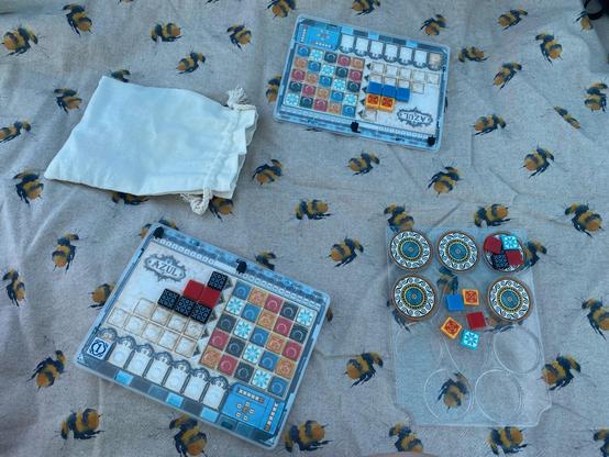 A very cute bumblebee picnic mat with two Azul Mini player boards, the shared draw pile for the tiles, and a fabric bag. It's a picture of a few turns in the game, so both player boards already have some tiles on.