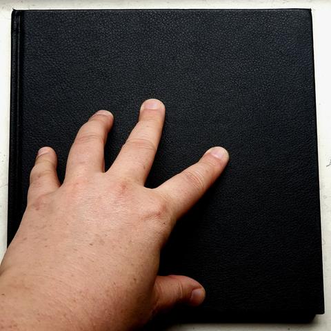 Foto einer Hand die auf einem quadratischen schwarzen Skiizenbuch ruht.
