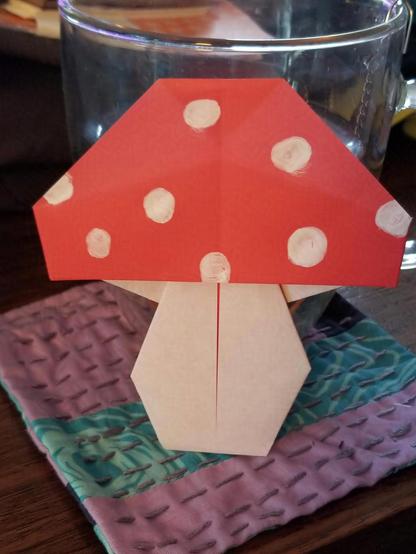 Photo of origami mushroom with white stem and red cap with white spots.