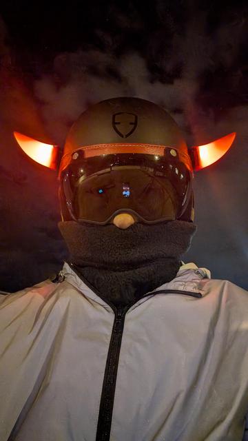 Selfie. Je porte un blouson gris réfléchissant, un tour de cou jusqu'au nez et un casque noir avec une visière miroir et deux cornes rouges lumineuses.