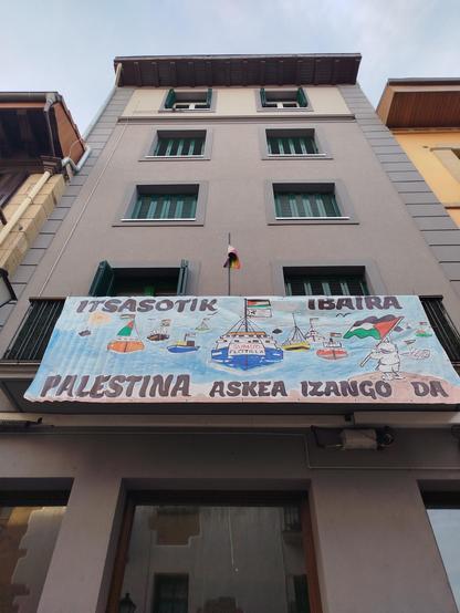 Herriko plazako etxebizitza bateko balkoian Global Sumud Flotillaren aldeko pankarta ilustratua.