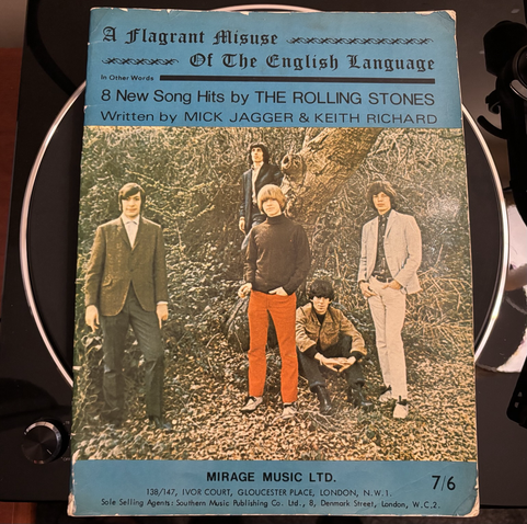 “A Flagrant Misuse Of The English Language - In Other Words - 8 New Song Hits by THE ROLLING STONES Written by MICK JAGGER & KEITH RICHARD” is the heading on a blue background with the boys pictured looking casual in the woods. With a price tag of the day printed at 7/6 (UK).