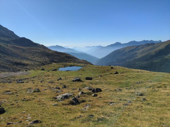 A very small lake in mountaineous grass landscape. The view to the far mountains is misted.
