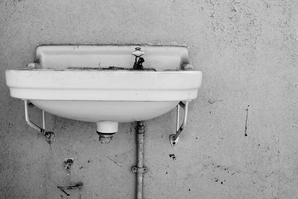 B&W-Aufnahme eines alten Waschbeckens in einer Barackenruine.