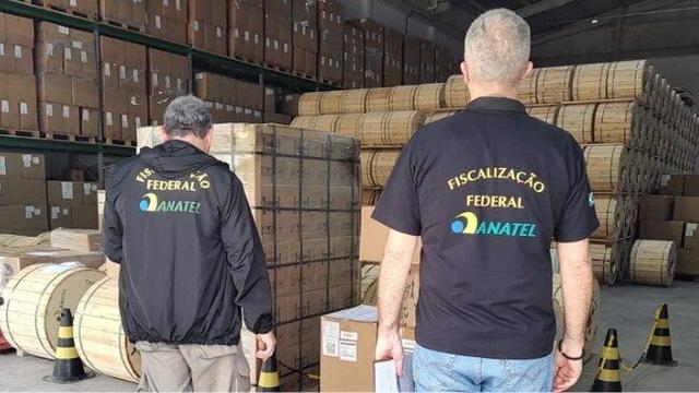 <figure class="wp-block-image size-full is-resized wp-lightbox-container"><img alt="Foto de dois agentes, vistos de costas, em um depósito ou galpão. Eles usam uniformes pretos com o logo da Agência Nacional de Telecomunicações (Anatel) e o texto &quot;Fiscalização Federal ANATEL&quot; em amarelo e azul" class="wp-image-854995" height="365" src="https://files.tecnoblog.net/wp-content/uploads/2025/10/operacao-de-fiscalizacao-da-anatel-edited.jpeg" style="width: 840px; height: auto;" width="649" /><button class="lightbox-trigger" type="button">
			<svg fill="none" height="12" viewBox="0 0 12 12" width="12" xmlns="http://www.w3.org/2000/svg">
				<path d="M2 0a2 2 0 0 0-2 2v2h1.5V2a.5.5 0 0 1 .5-.5h2V0H2Zm2 10.5H2a.5.5 0 0 1-.5-.5V8H0v2a2 2 0 0 0 2 2h2v-1.5ZM8 12v-1.5h2a.5.5 0 0 0 .5-.5V8H12v2a2 2 0 0 1-2 2H8Zm2-12a2 2 0 0 1 2 2v2h-1.5V2a.5.5 0 0 0-.5-.5H8V0h2Z" fill="#fff">
			</svg>
		</button><figcaption class="wp-element-caption">Operação da Anatel recolheu produtos sem homologação (imagem: reprodução/Anatel)</figcaption></figure>


<details class="tb-resumo tb-callout padrao">
    Resumo
    <div class="tb-resumo-topicos tb-callout-texto"><ul>
<li>A Anatel apreendeu 1,7 milhão de metros de cabos de fibra óptica irregulares em São Paulo.</li>
<li>A operação ocorreu entre 23 e 26 de setembro na Bahia, São Paulo, Paraíba e Santa Catarina.</li>
<li>Foram lacrados produtos sem homologação, incluindo carregadores, fones, roteadores e fechaduras eletrônicas.</li>
</ul>
</div>
</de