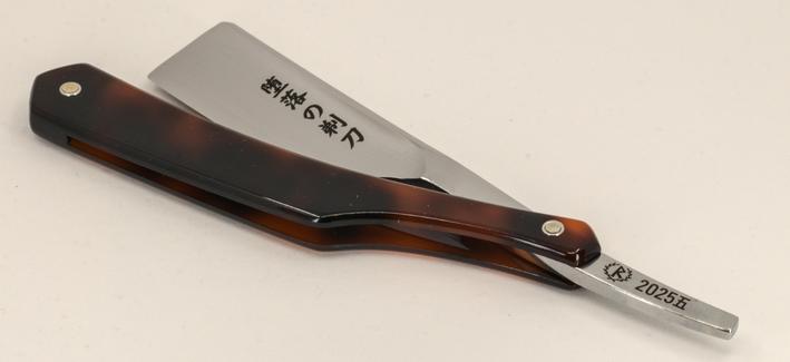 (Le Chat Mistral description)

This image shows a traditional straight razor, folded and resting on a light-coloured surface. The razor has a polished, metallic blade and a tortoiseshell-patterned handle with dark and light brown tones. The blade is etched with Japanese characters that read "堕落の剃刀", which translates to "The Depraved Razor" or "Razor of Depravity". Near the base of the blade, there is a marking that includes "2025.五", indicating May 2025. The razor appears well-crafted and designed for precision shaving.
