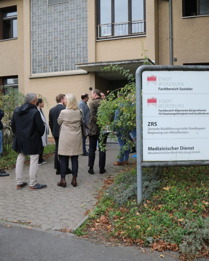 Gruppe von Menschen außerhalb eines Gebäudes mit einem Schild für den Fachbereich Soziales der Stadt Würzburg.