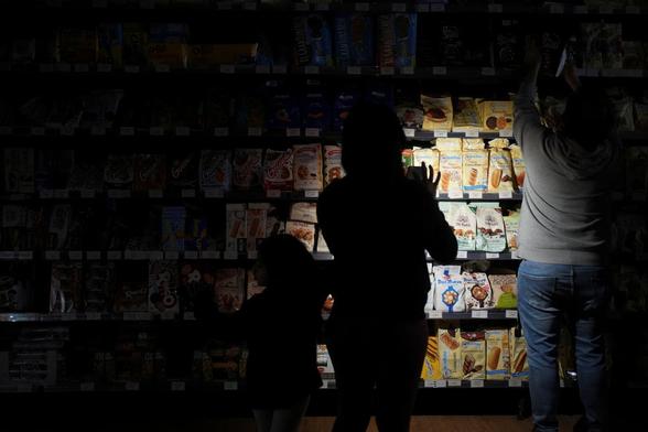 Unas personas usan la linterna del teléfono para hacer la compra en un supermercado de Barcelona, el 28 de abril de 2025. (Bruna Casas / REUTERS)