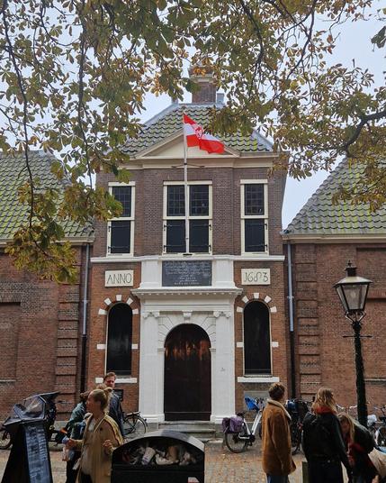 The front entrance in classicist style of the Jean Pesijn alms court in Leiden. It's october 3 so the city flag is flying. Nearly all the windows are shuttered. People are parking their bikes to visit the children's fairground.
