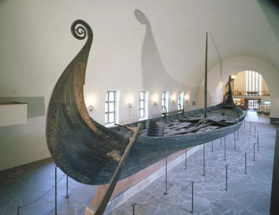 The Oseberg Ship in the former Viking Ship Museum.
Museum of the Viking Age/University of Oslo 

A wooden ship with curly ends and a single mast, just like those art works we all remember.

Seen here inside a large, bright, whitewashed-walled exhibit hall.