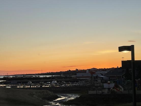Shot of a predominantly orange sunrise with water and some boats.