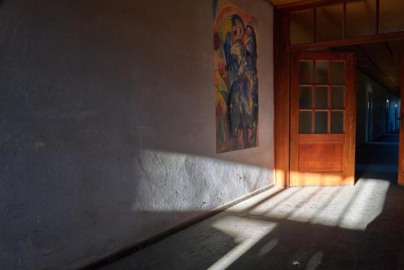 Ein dunkler Flur in einer der Baracken der Gedenkstätte. Der Flur wird durch eine rötliche Pendeltür geteilt. An der Flurwand befindet sich die Replica eines der berühmten Bilder mit den blauen Pferden von Franz Marc.