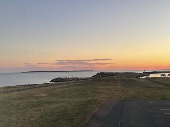 Photo of a sunrise over a large body’s of water with an expanse of grass in the foreground.