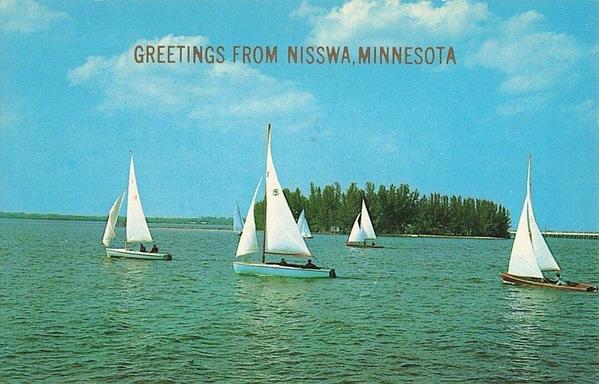 Sail boats , sailing from right to left. There is a small island with tall conifers in the background.