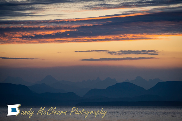 Pre-dawn sun illuminating clouds over a mountain chain.