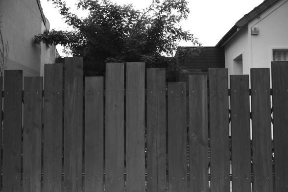 A black and white photo of a part of a wooden fence but each plank is not straighten out with its neighbours