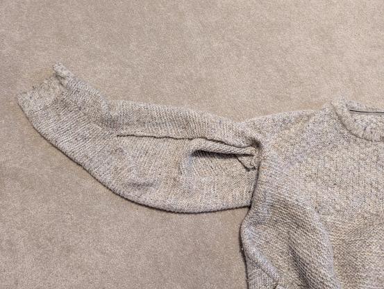 1) A photo of a grey/white marled jumper lying on a brown carpet, showing a massive hole along the seam of the right sleeve, running from the body join about 2/3 the length of the sleebe.