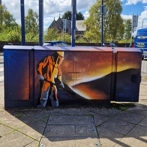 Utility box mural in Clydach depicting an iron worker, celebrating the village’s industrial history as part of Swansea’s street art project.